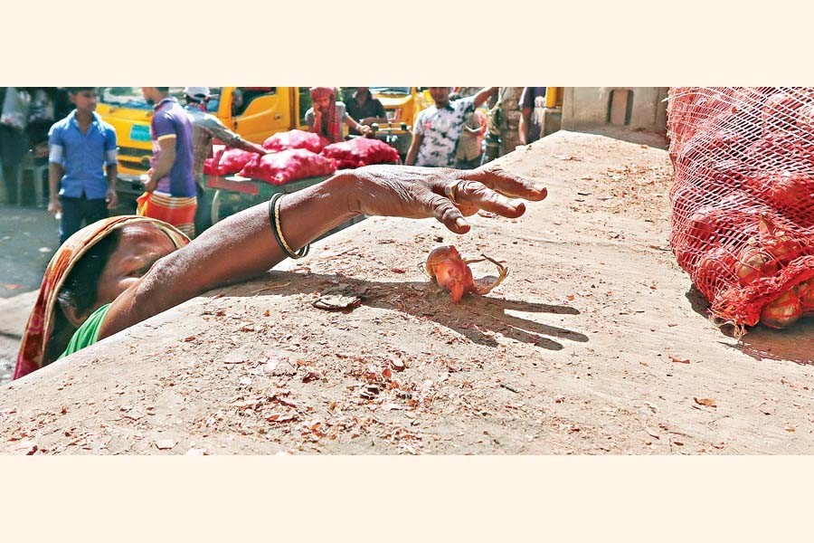 A poor woman reaching out to an onion that dropped from a sack while loading it onto a truck at the Shyambazar wholesale market in the capital on Monday — FE Photo by Shafiqul Alam
