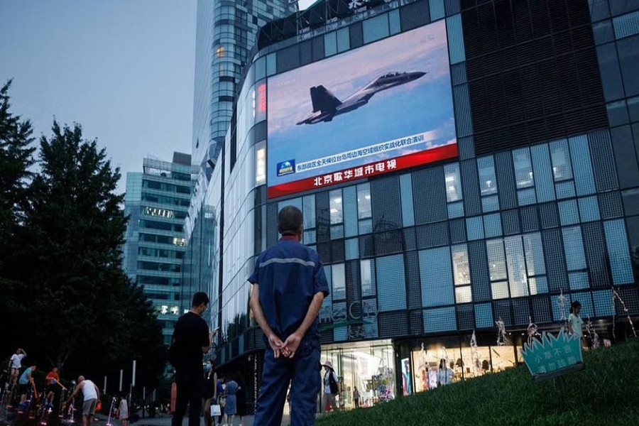তাইওয়ানের কাছে চীনের সর্বাত্মক সামরিক মহড়া চলাকালে একটি জঙ্গি বিমান উড়ে যাচ্ছে; বেইজিংয়ের একটি মার্কেটের সামনের টেলিভিশন স্ক্রিনে সিসিটিভির খবরে সেটি দেখছেন এক ব্যক্তি। ছবি: রয়টার্স