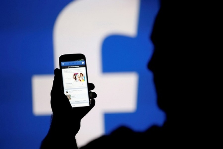 A man is silhouetted against a video screen with a Facebook logo as he poses with an Samsung S4 smartphone in this photo illustration Aug 14, 2013. Reuters