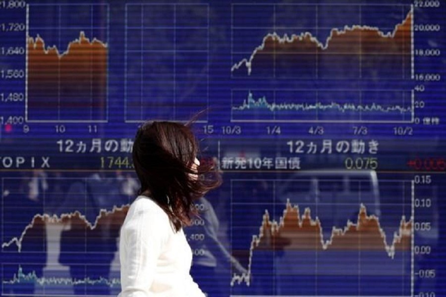 A woman walks in strong wind caused by Typhoon Lan, past an electronic board showing the graphs of the recent movements of Japan's Nikkei average outside a brokerage in Tokyo, Japan, October 23, 2017. Reuters