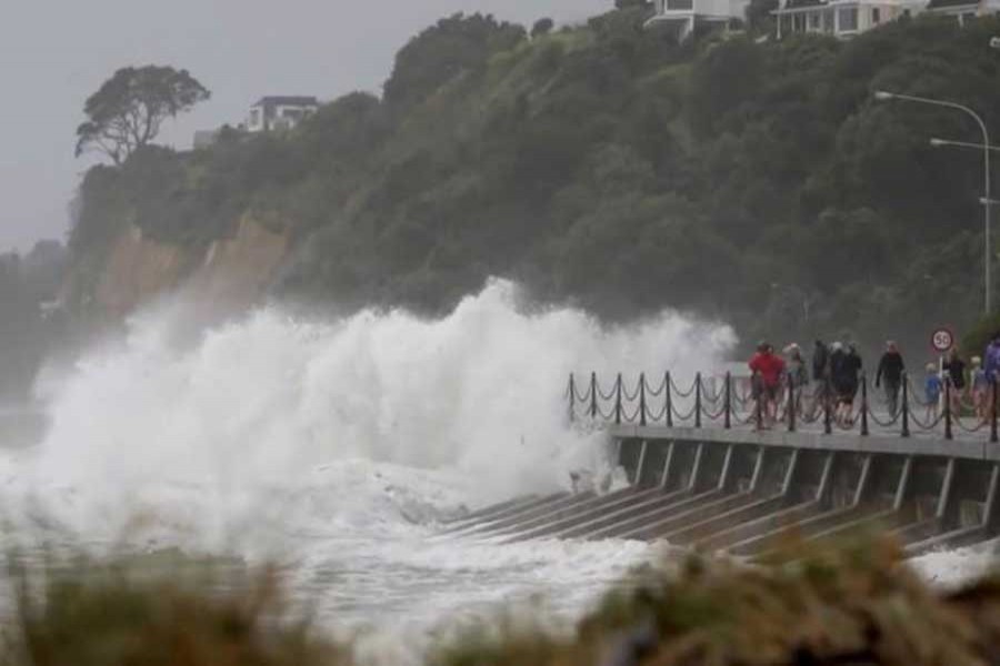 A wave crashes on the shore as people walk along a road in Nelson, after former Tropical Cyclone Fehi descended upon New Zealand, in this still image taken from a February 1, 2018 social media video. Reuters