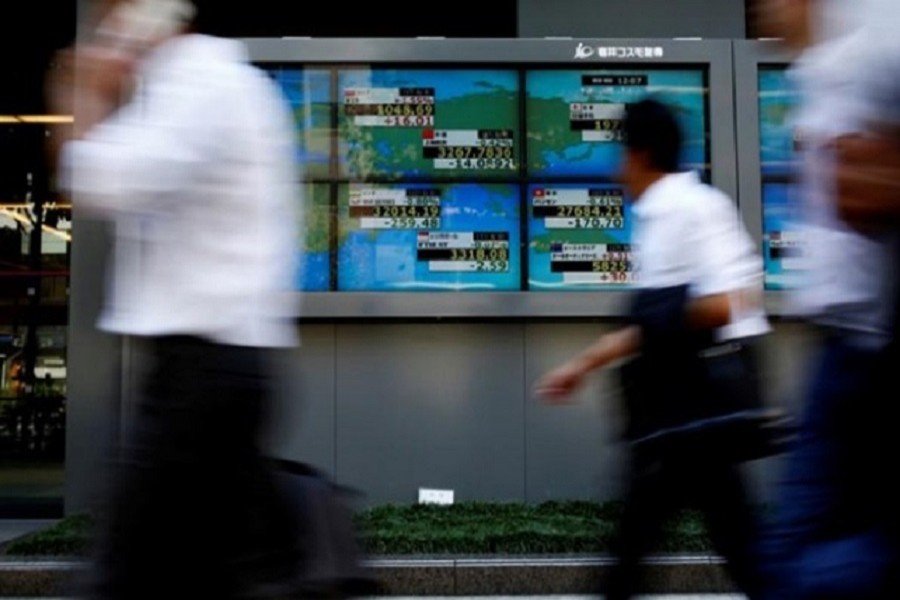 People walk past an electronic board showing Japan's Nikkei average outside a brokerage at a business district in Tokyo, Japan August 9, 2017. Reuters/Files