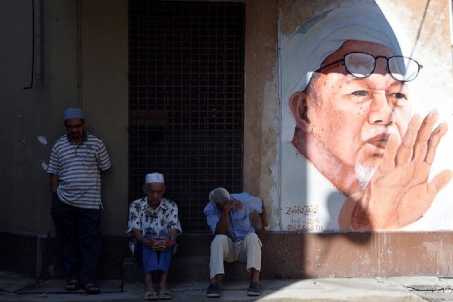 People sit next to a mural of the late former Party Islam Se-Malaysia (PAS) president, Tuan Guru Nik Abdul Nik Mat at Medan Ilmu in Kota Bharu, Kelantan, Malaysia April 13, 2018. Reuters