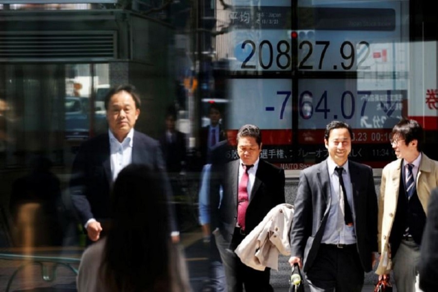 People walk past an electronic board showing Japan's Nikkei average outside a brokerage in Tokyo, Japan, March 23, 2018. Reuters/Files