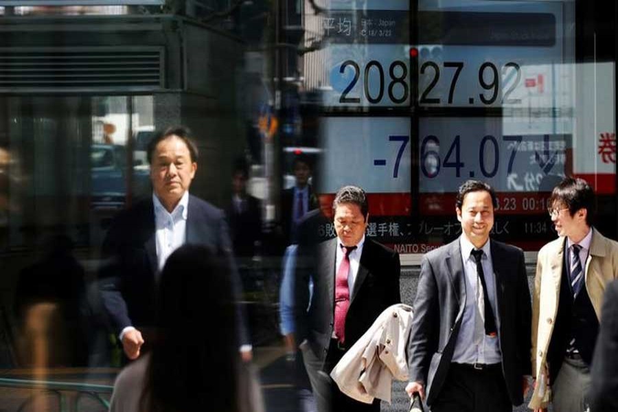 People walk past an electronic board showing Japan's Nikkei average outside a brokerage in Tokyo, Japan, March 23, 2018. Reuters/Files