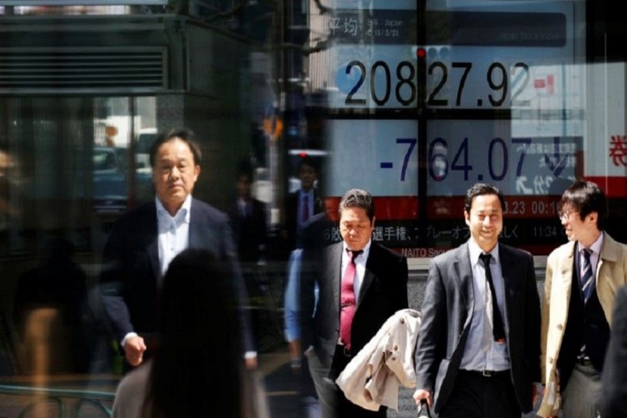 People walk past an electronic board showing Japan's Nikkei average outside a brokerage in Tokyo, Japan, March 23, 2018. Reuters/Files