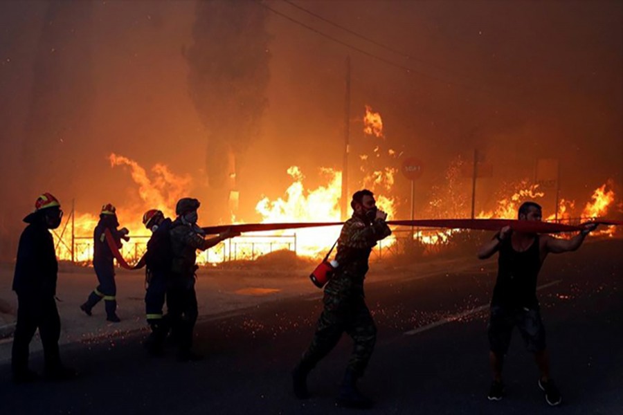 Firefighters, soldiers and local residents carry a hose as a wildfire burns in the town of Rafina, near Athens, Greece on Monday — Reuters