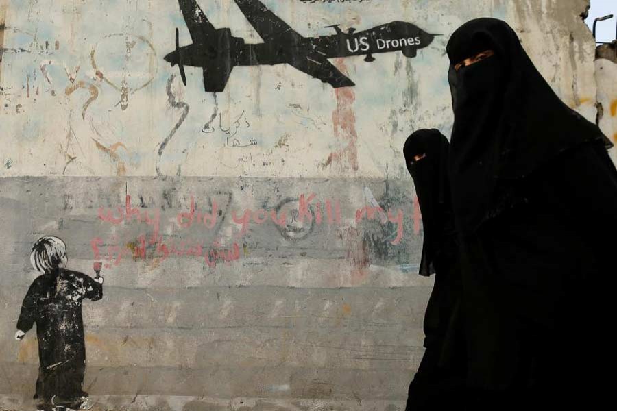 Women walk past a graffiti, denouncing strikes by US drones in Yemen, painted on a wall in Sanaa, Yemen February 6, 2017. Reuters/Files