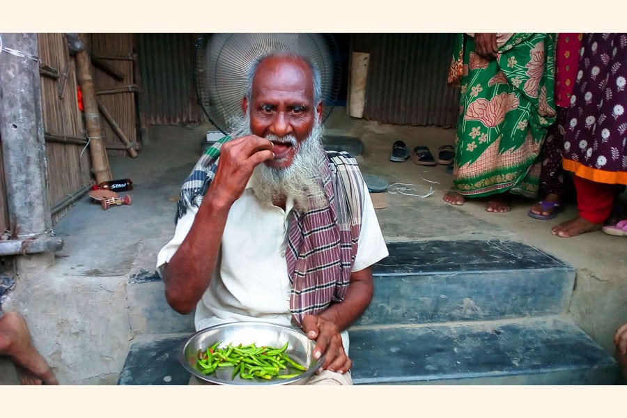 Mobarak Mollah eating green chilli at his home	— FE Photo