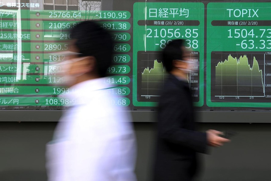 People wearing protective face masks, following an outbreak of the coronavirus, walk past a screen showing Nikkei index, outside a brokerage in Tokyo, Japan on February 28, 2020 — Reuters photo