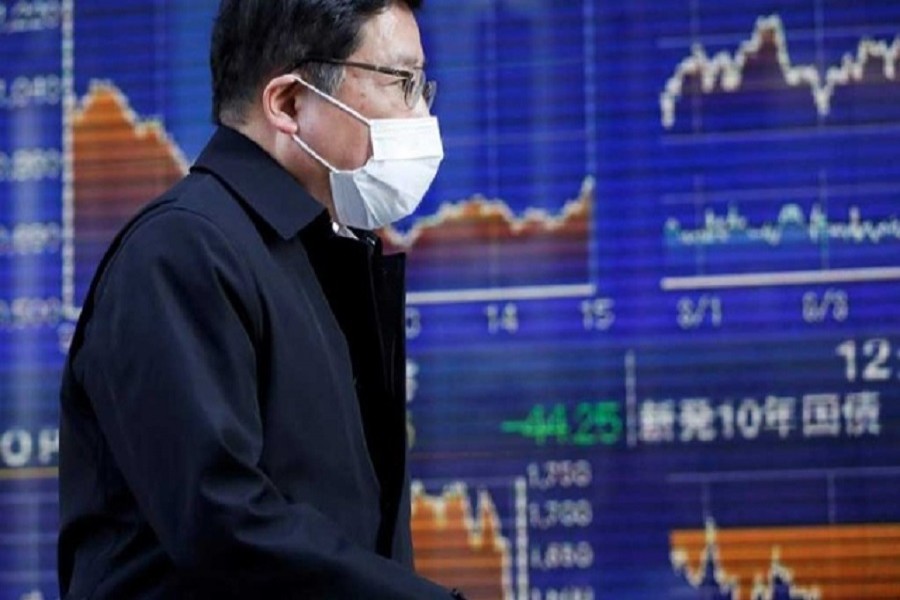 A passerby wearing a protective face mask, following an outbreak of the coronavirus, walks past an electronic board showing the graphs of the recent movements of Japan's Nikkei share average outside a brokerage in Tokyo, Japan, March 06, 2020. — Reuters/Files