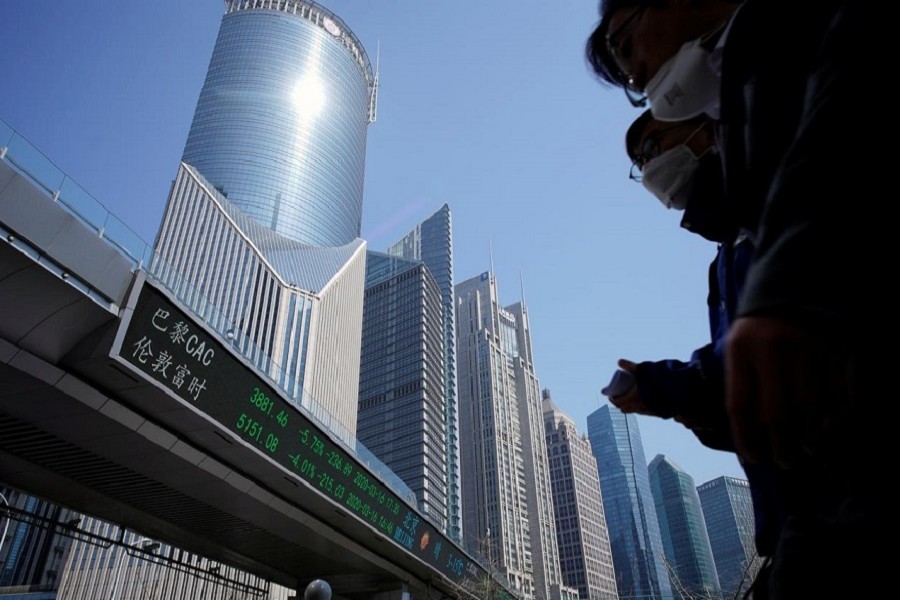 Pedestrians wearing face masks walk near an overpass with an electronic board showing stock information, following an outbreak of the coronavirus disease (COVID-19), at Lujiazui financial district in Shanghai, China, March 17, 2020 – Reuters/Files