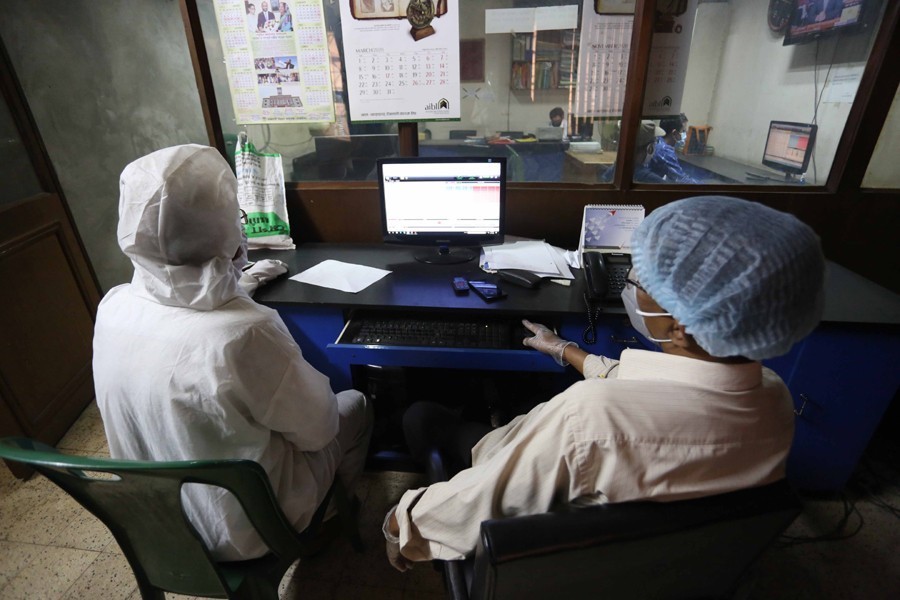 Traders, in protective suits, monitoring stock price movements on computer screens at a brokerage house in the capital city — FE/Files