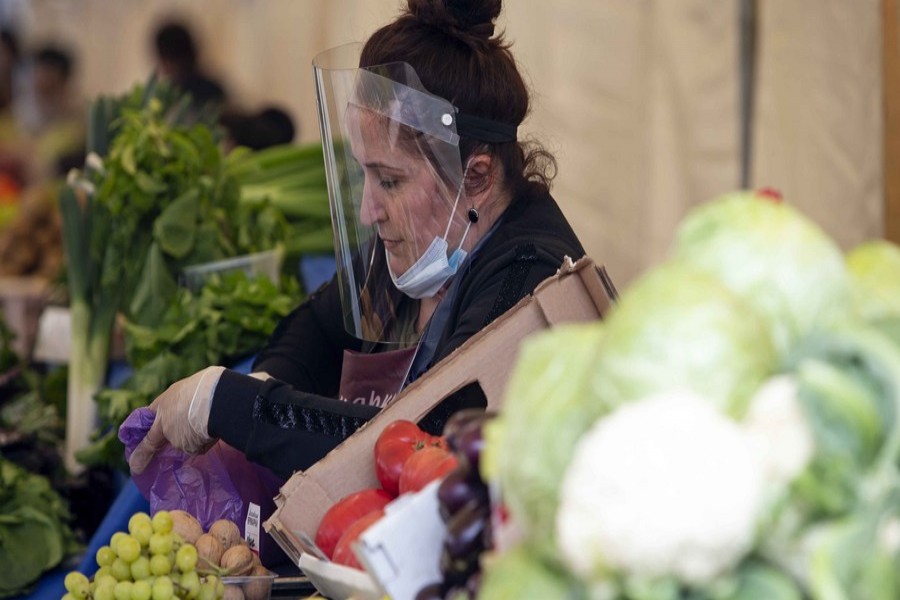 A street vendor wearing a face shield and gloves picks fruits for a customer at a street market in Moscow, Russia, on June 5, 2020. (Photo by Alexander Zemlianichenko Jr/Xinhua)