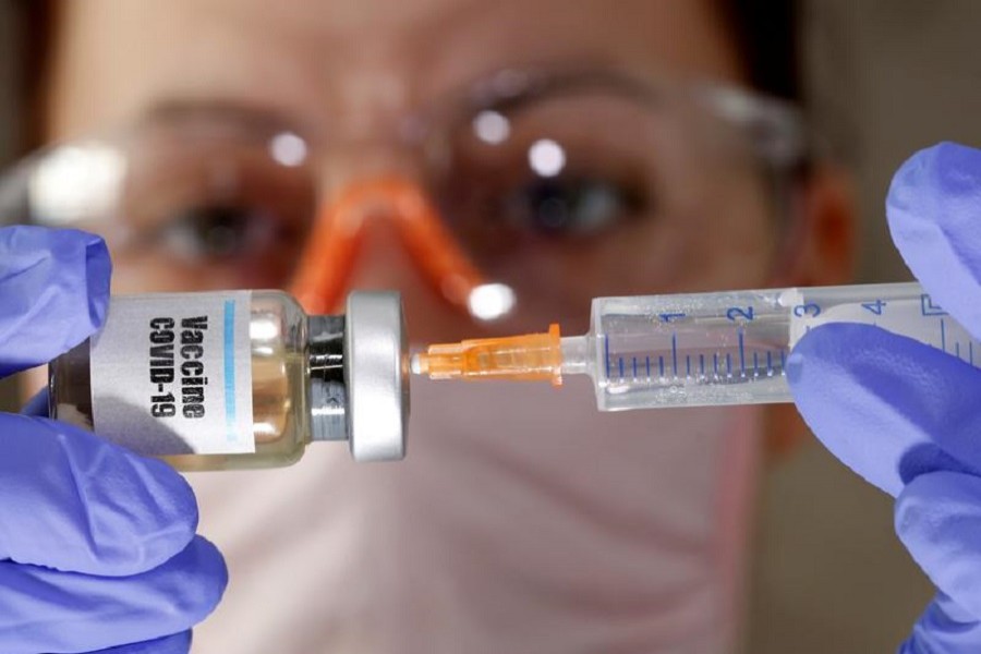 A woman holds a small bottle labeled with a "Vaccine COVID-19" sticker and a medical syringe in this illustration taken April 10, 2020 — Reuters/Illustration