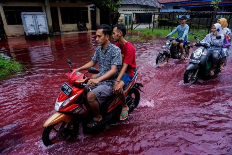 People ride motorbikes through a flooded road with red water due to the dye-waste from cloth factories, in Pekalongan, Central Java province, Indonesia on February 6, 2021 — Antara Foto via Reuters