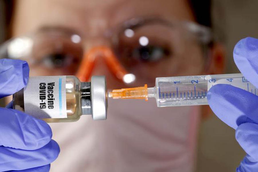 A woman holds a small bottle labelled with a "Vaccine COVID-19" sticker and a medical syringe in this illustration taken April 10, 2020 — Reuters/Files