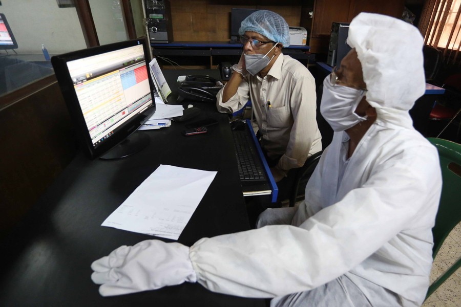 Investors, in protective suits, monitoring stock price movements on computer screens at a brokerage house in the capital city — FE/Files