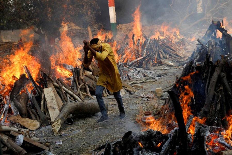 A man runs past the burning funeral pyres of those who died from the coronavirus disease (COVID-19), during a mass cremation, at a crematorium in New Delhi, India April 26, 2021. REUTERS/Adnan Abidi