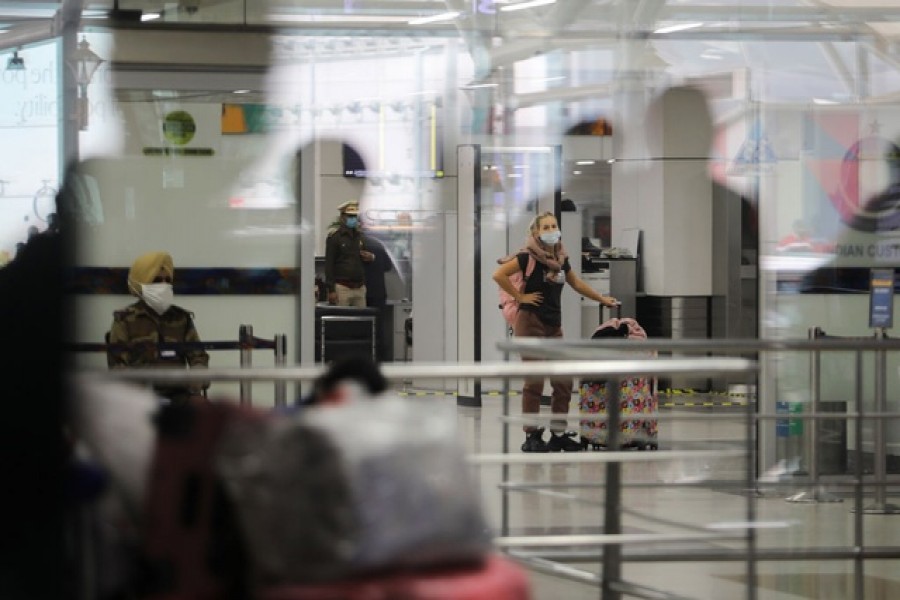 A woman wearing a protective face mask waits with her luggage inside the arrival section of the Indira Gandhi International Airport in New Delhi, India, Dec 3, 2021. REUTERS/Anushree Fadnavis