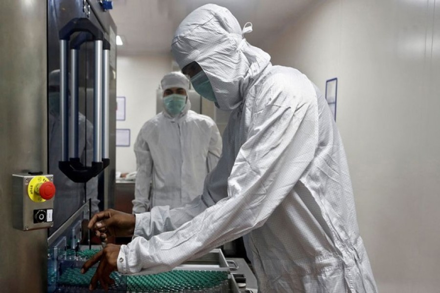 An employee in personal protective equipment (PPE) removes vials of AstraZeneca's COVISHIELD, coronavirus disease (COVID-19) vaccine from a visual inspection machine inside a lab at Serum Institute of India, Pune, India, November 30, 2020 – Reuters/Files