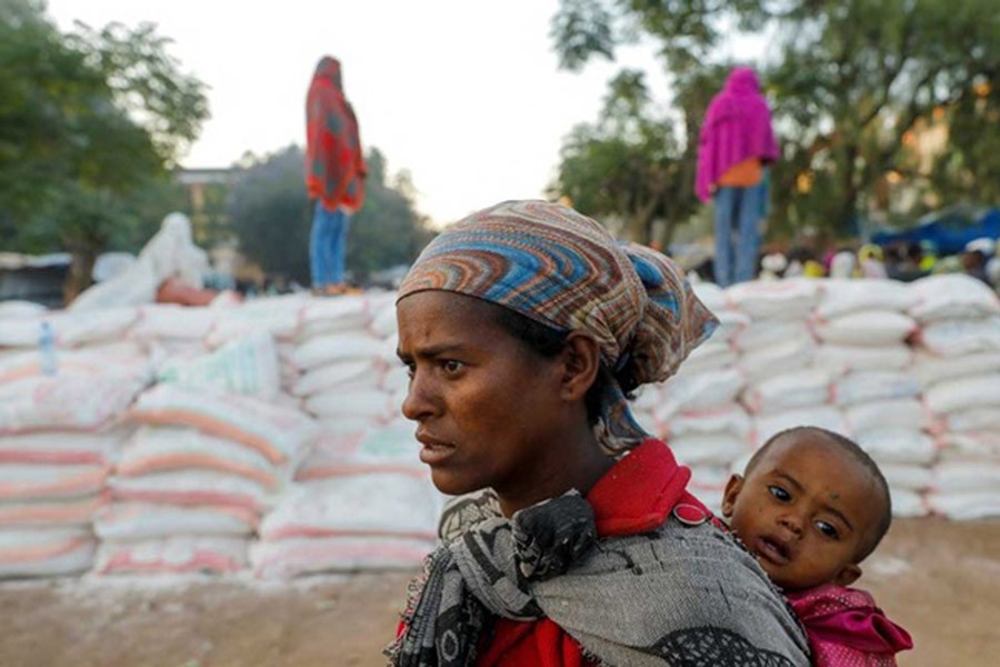 A woman carries an infant as she queues in line for food, at the Tsehaye primary school, which was turned into a temporary shelter for people displaced by conflict, in the town of Shire, Tigray region, Ethiopia, Mar 15, 2021. REUTERS/Baz Ratner/File