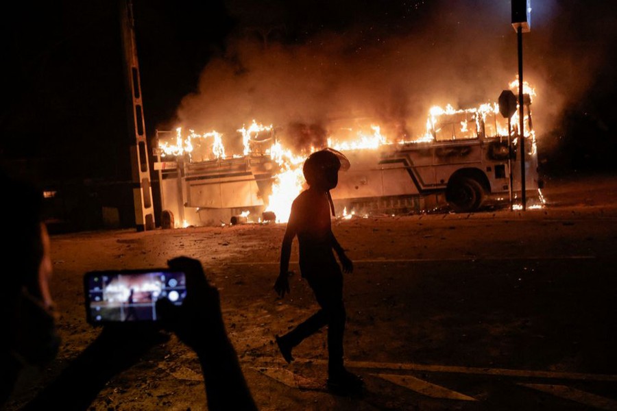 A person takes a photo as a demonstrator walks near a bus that was set on fire at the top of the road to Sri Lankan President Gotabaya Rajapaksa's residence during a protest against him as many parts of the crisis-hit country faced up to 13 hours without electricity due to a shortage of foreign currency to import fuel, in Colombo, Sri Lanka on March 31, 2022 — Reuters photo