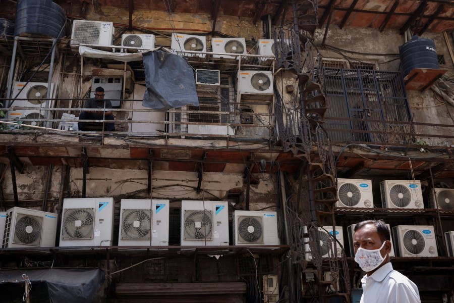 A man uses his mobile phone as he sits amidst the outer units of air conditioners, at the rear of a commercial building in New Delhi, India on April 30, 2022 — Reuters photo