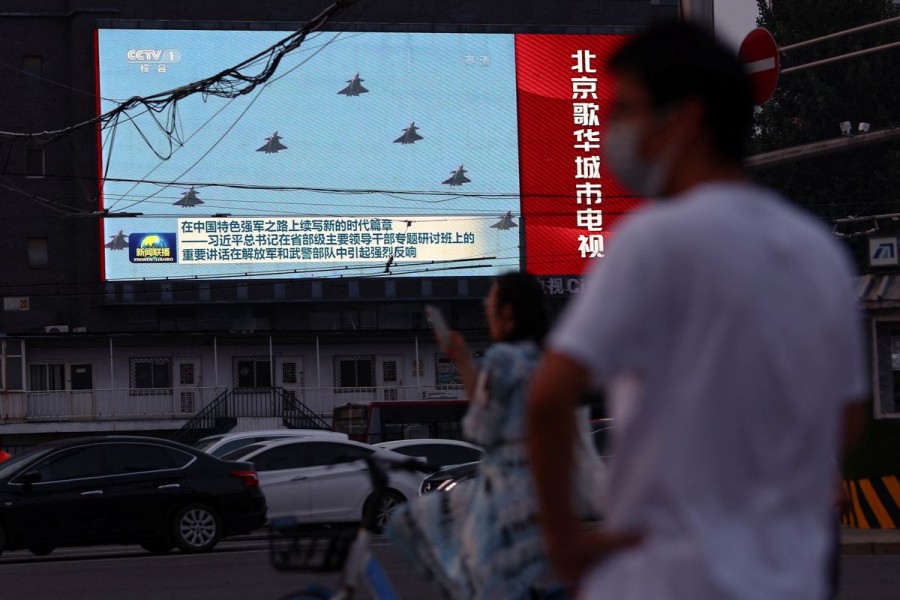 Pedestrians wait at an intersection near a screen showing footage of Chinese People's Liberation Army (PLA) aircraft during an evening news programme, in Beijing, China August 2, 2022. REUTERS/Tingshu Wang