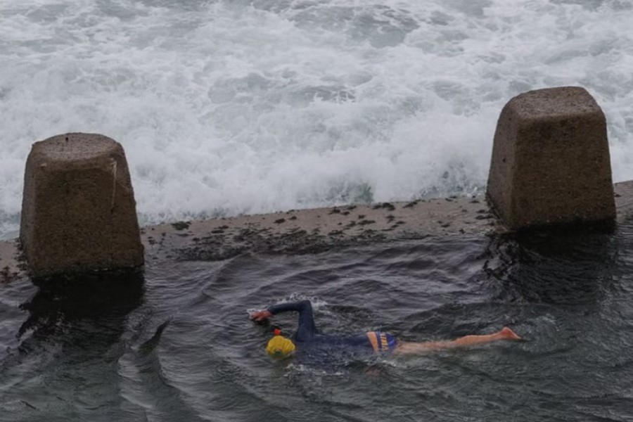 A person swims in a rock pool while large waves approach at Coogee Beach, as heavy rains affect Sydney, Australia, October 6, 2022. REUTERS