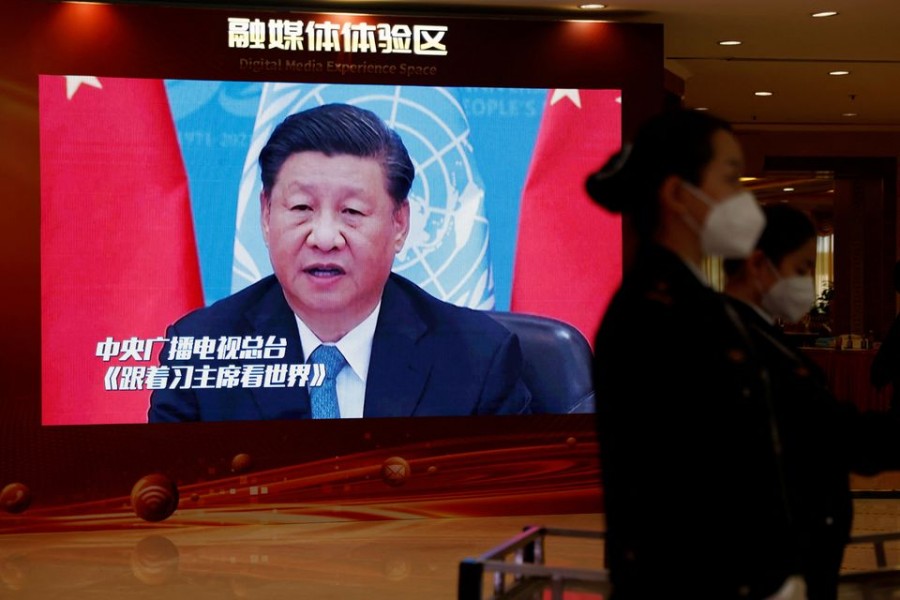 Staff members, wearing face masks following the coronavirus disease (COVID-19) outbreak, stand near a screen displaying an image of Chinese President Xi Jinping, inside a media hotel for journalists covering the 20th National Congress of the Communist Party of China in Beijing, China October 19, 2022. REUTERS/Tingshu Wang