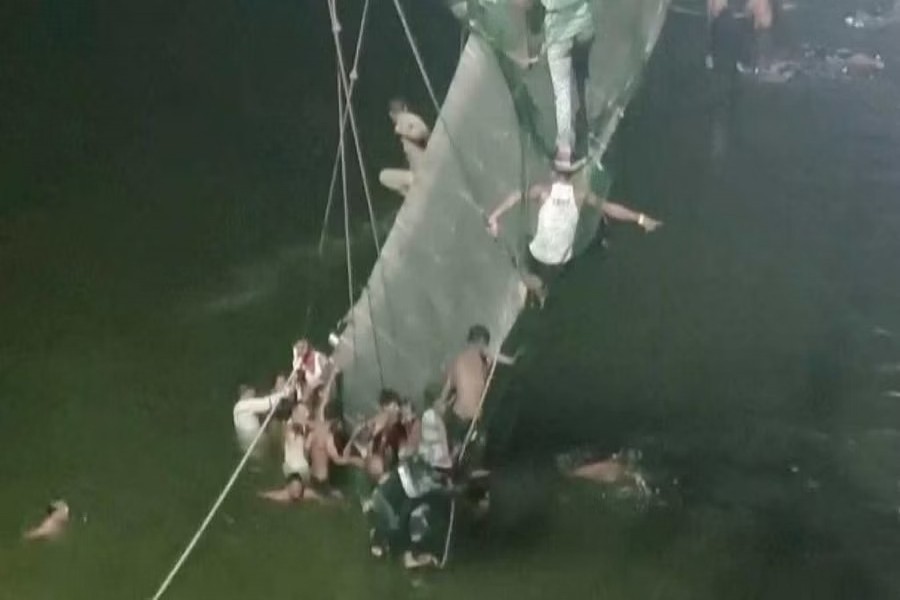 People cling on to the collapsed suspension bridge in Morbi, India October 30, 2022 in this screen grab obtained from a video. ANI/ Handout via REUTERS